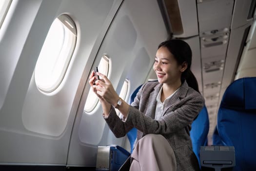 Young female traveler sits near the window in first class on a plane during a flight. Use your cell phone to take photos of the view outside your window, travel, and business ideas..