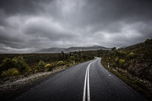 The picturesque Gordon River Rd at the Sentinel range of mountains near Bitumen Bones Sculpture on a cool wet summer's morning in Southwest National Park, Tasmania, Australia