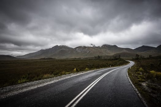 The picturesque Gordon River Rd at the Sentinel range of mountains near Bitumen Bones Sculpture on a cool wet summer's morning in Southwest National Park, Tasmania, Australia