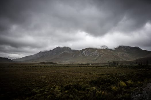 The picturesque Gordon River Rd at the Sentinel range of mountains near Bitumen Bones Sculpture on a cool wet summer's morning in Southwest National Park, Tasmania, Australia