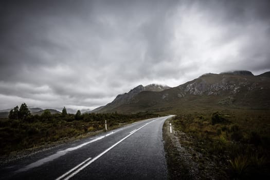 The picturesque Gordon River Rd at the Sentinel range of mountains near Bitumen Bones Sculpture on a cool wet summer's morning in Southwest National Park, Tasmania, Australia