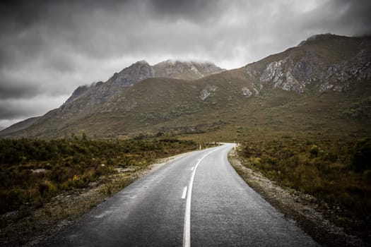 The picturesque Gordon River Rd at the Sentinel range of mountains near Bitumen Bones Sculpture on a cool wet summer's morning in Southwest National Park, Tasmania, Australia