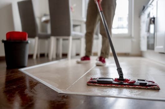 Woman Mops Floor In Kitchen With Broom Prominently In Foreground