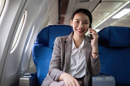 Young woman talking on the phone, communicating on business before traveling Sitting near window in first class on airplane during flight, travel and business concept..