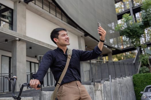 A young Asian businessman rides a bicycle to work. Standing outside the office talking on the phone and talking about business. Concept of reducing energy and reducing air pollution..