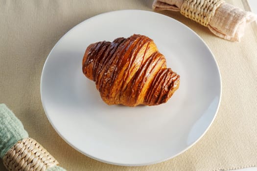 Croissant delicately placed on a pristine white plate, showcasing its buttery layers and inviting aroma.