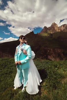 A young man and his wife stand in an embrace high in the mountains against the backdrop of epic rocks on a sunny day. Newlyweds wedding couple in the mountains.