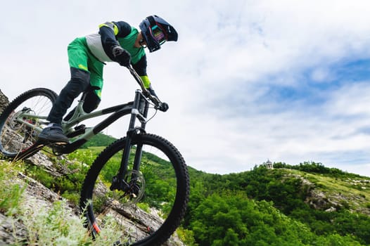 Professional cycling. Downhill descent from the mountains by bicycle. Young rider going down the mountain on a mountain bike in summer surrounded by greenery.