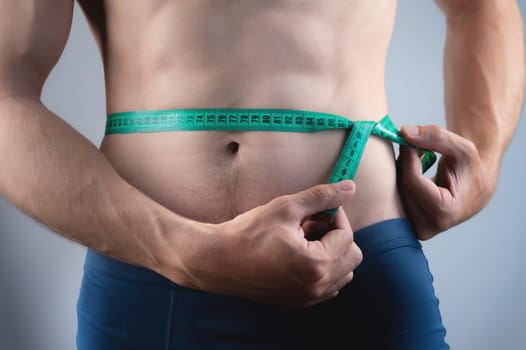 Close-up of the bare torso and waist area with a measuring tape. A man of average build controls his belly size.