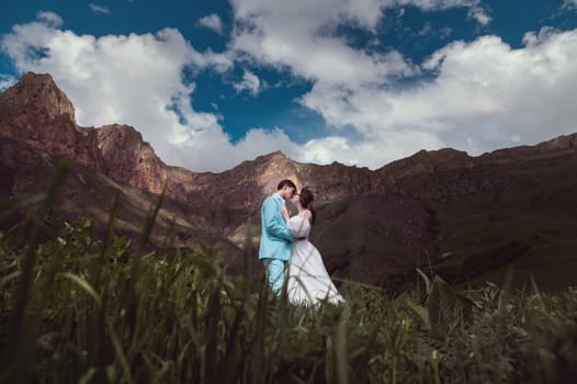 A young man and his wife stand in an embrace high in the mountains against the backdrop of epic rocks on a sunny day. Newlyweds wedding couple in the mountains.
