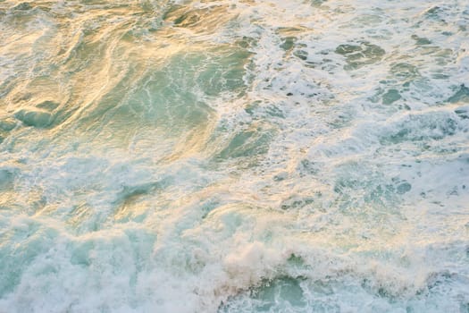 A closeup shot of the ocean with wind waves crashing onto the shore, creating a beautiful pattern of furrows in the water. The landscape is enhanced by cumulus clouds in the sky