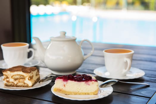 Afternoon tea set with hot tea and tasty cakes on the table and the swimming pool. Hotel resort or resting concept