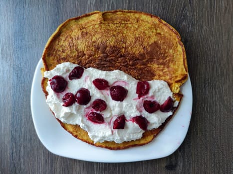 oat pancake with cottage cheese and cherries on a white plate.