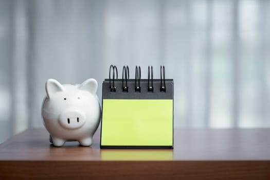 Piggy bank and notepad on a wooden table with copy space, embodying the concept of combining financial mindfulness with thoughtful planning and the potential for recording ideas or goals.