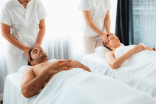 Caucasian couple enjoying relaxing anti-stress head massage and pampering facial beauty skin recreation leisure in dayspa modern light ambient at luxury resort or hotel spa salon. Quiescent