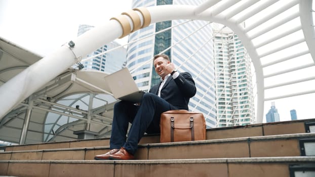 Low angle view of professional business man working on laptop at stairs while celebrate successful project. Caucasian project manager using computer to plan marketing strategy at urban city. Urbane.