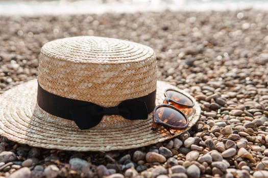 A straw hat and sunglasses on the beach. Pebbles on the seashore, close-up. The natural background.