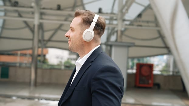 Happy business man using headphone listening relax music and move along music while walking at street in urban city with lively mood. Manager wear headset and enjoying listen relaxing rhyme. Urbane.