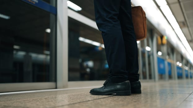 Skilled caucasian business man standing or waiting for train while holding bag. Closeup image of smart project manager leg standing at door area. Represented public transport, waiting, rule. Exultant.