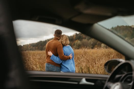 View through the car window, a man and woman are embracing each other, adult couple enjoying their road trip