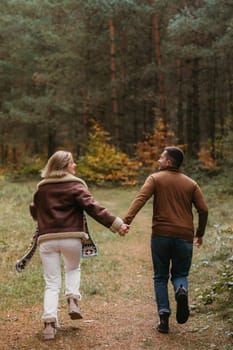 Adult couple having fun together in autumn park, man and a woman are holding hands while running through the woods