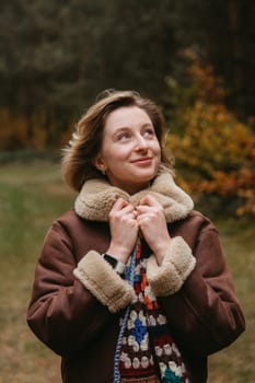 Happy caucasian woman in brown jacket is standing in the autumn woods and cheerfully looking up