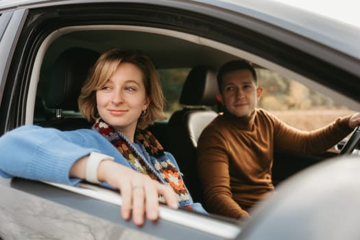 Adult couple on autumn road trip, man and woman sitting in the car and looking through the window
