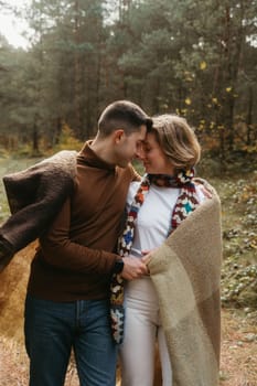 A man and woman covered in a blanket snuggled up to each other in the middle of the forest, a couple enjoying time together outside the city