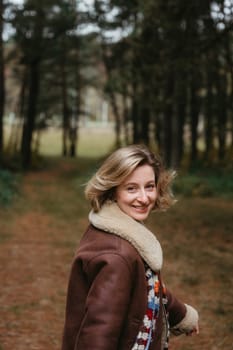 Happy and cheerful adult caucasian woman in a brown jacket is walking through autumn forest