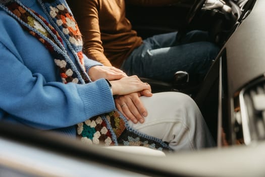 Two individuals are seated in a vehicle, with their fingers intertwined, showing a gesture of comfort and connection while traveling together