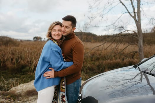 happy man and woman are embracing in front of a car, with smiles on their faces