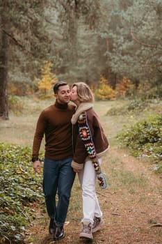 A woman is kissing man on the cheek while walking through autumn forest, happy couple spending time together