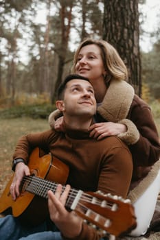 A man plays guitar and woman hugs him from behind in autumn park outdoors