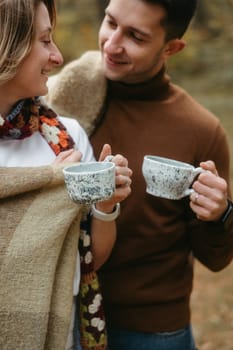 Man and woman outdoors standing together smiling, holding handmade ceramic tea cups