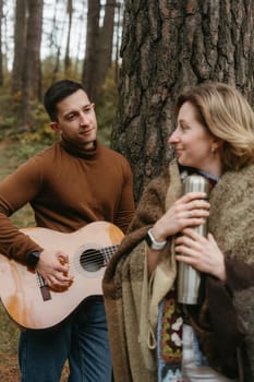 A man is playing a guitar for woman in the woods in autumn, adult couple spending time together