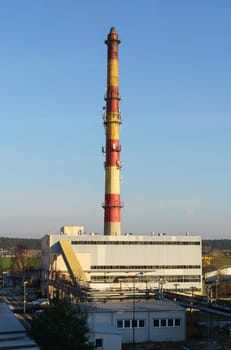 A factory building featuring a prominent red and yellow tower, standing tall against the sky. Vertical frame.