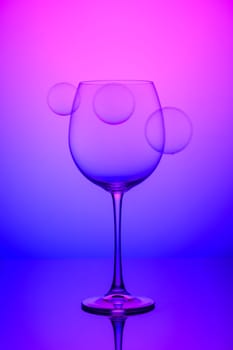 wine glass with soap bubbles on blue and pink background