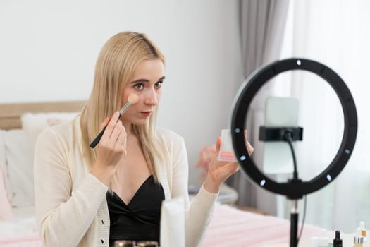 Young woman making beauty and cosmetic tutorial video content for social media. Beauty blogger smiles to camera while showing how to apply mascara to audience or followers. Blithe