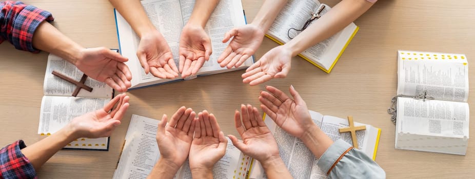 Cropped image of diversity people hand praying together at wooden church on bible book. Group of believer hold hand together faithfully. Concept of hope, religion, faith, god blessing. Burgeoning.