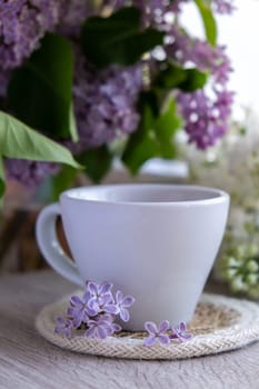 Tasty black tea in white cup on windowsill with aromatic lilac flowers. Spring composition Cup of lilac tea drinking recipe flowering branches of purple lilac. Still life for copy space greeting card, poster, banner, wallpaper. Relaxation and natural ingredients