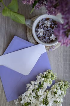 Empty envelope copy space paper note with Tasty black tea in white cup on windowsill with aromatic lilac flowers. Spring composition Cup of lilac tea drinking recipe flowering branches of purple lilac. Still life for greeting card, poster, banner, wallpaper. Relaxation and natural ingredients