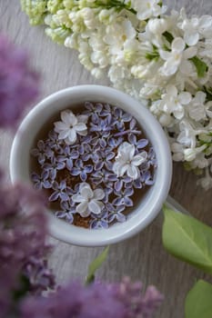 Tasty black tea in white cup on windowsill with aromatic lilac flowers. Spring composition Cup of lilac tea drinking recipe flowering branches of purple lilac. Still life for copy space greeting card, poster, banner, wallpaper. Relaxation and natural ingredients