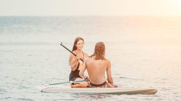 Sea woman and man on sup. Silhouette of happy young woman and man, surfing on SUP board, confident paddling through water surface. Idyllic sunset. Active lifestyle at sea or river