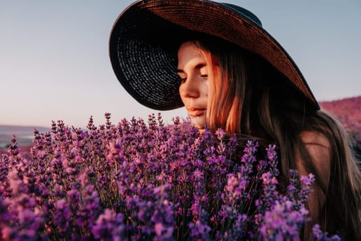 Close up portrait of young beautiful woman in a white dress and a hat is walking in the lavender field and smelling lavender bouquet.