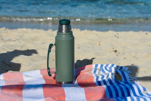 Authentic green Stanley Thermos on the beach in summer.