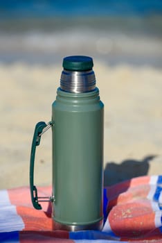 Authentic green Stanley Thermos on the beach in summer.