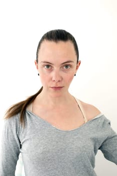 Young adult woman with a ponytail and combed hair looks at the camera photo at documents in a gray sweater with an open shoulder on a white background