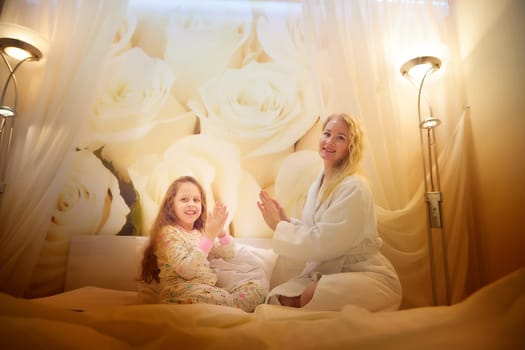 Mother and daughter having relax, fun, play together on bed in bedroom. The concept of tenderness between mom and girl