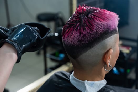 The hairdresser dyes the hair of an Asian woman in pink. Short extreme haircut