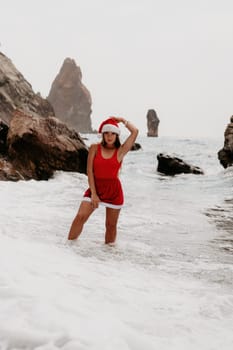 Woman travel sea. Young Happy woman in a long red dress posing on a beach near the sea on background of volcanic rocks, like in Iceland, sharing travel adventure journey